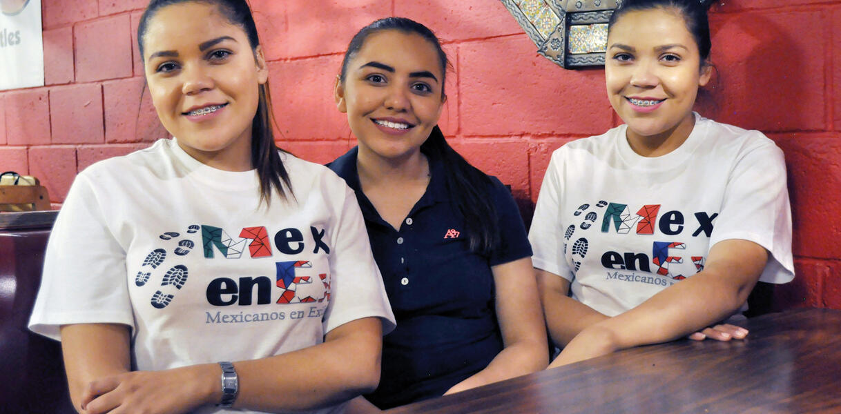 Die drei Schwestern Citlali, Deisy und Paola Alvarado sitzen lächelnd  nebeneinander an einem Tisch, zwei von ihnen sind eineiige Zwillinge