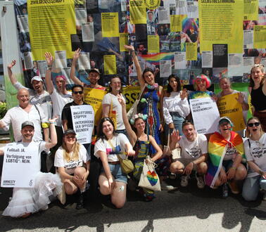 Eine Gruppe von 18 Personen posiert lächelnd vor einem Lastwagen, dessen Seiten mit Amnesty-Plakten beklebt sind.