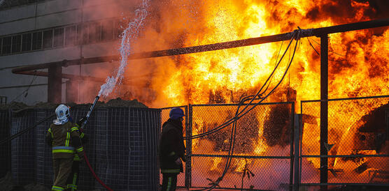 Das Bild zeigt wie ein Gebäude brennt, Feuerwehrkräfte versuchen den Brand zu löschen