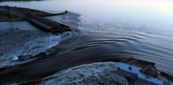 Das Bild zeigt, wie riesige Wassermassen eines Stausees durch einen zerstörten Staudam, fließen