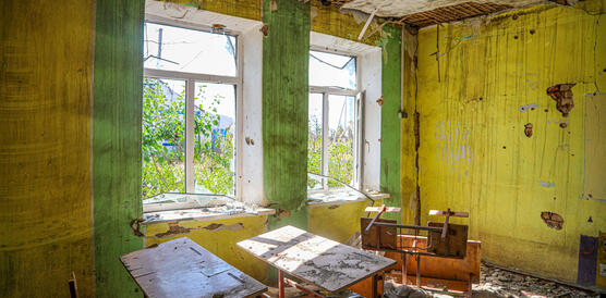 Das Foto zeigt ein Klassenzimmer mit zerstörten Decken und Wänden und Schmutz auf den Tischen.