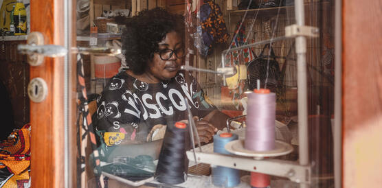 Eine nigerianische Frau sitzt an einer Nähmaschine, sie trägt eine Hornbrille, das Haar fällt lockig in ihren Nacken.