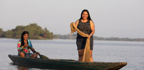 Das Bild zeigt zwei Frauen auf einem schmalen Fischerboot, sie lächeln in die Kamera