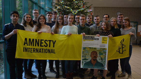 Schülerinnen und Schüler halten ein Amnesty-Banner und ein Plakat zu Tadjadine Mahamat Babouri in die Kamera