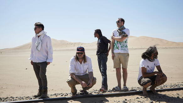Fünf Männer stehen oder hocken in der Wüste