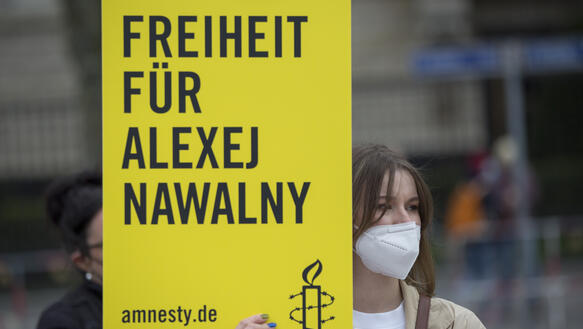 Das Bild zeigt eine Maske-tragende Frau, die vor der russischen Botschaft steht und ein Schild mit den Worten "Freiheit für Alexej Nawalny"  vor sich hält.
