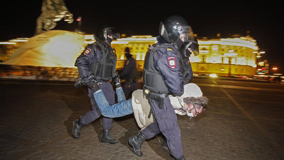 Das Bild zeigt zwei Polizisten, wie sie eine Person an Händen und Füßen wegtragen