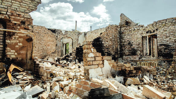 Die Ruine eines Hauses, das vollkommen zerstört wurde, über die eingestürzten Backsteinmauern spannt sich der Himmel, an dem ein paar Wolken hängen.