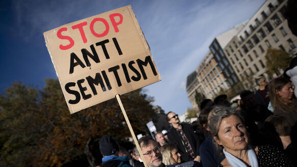 Das Foto zeigt einen Mann inn einer Menschenmenge, der ein Schild hochhält, auf dem steht: "Stop Antisemitism".