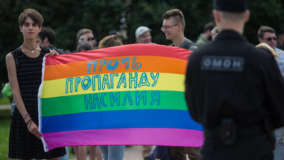 Das Bild zeigt mehrere Menschen, manchen halten eine Regenbogenfahne in der Hand
