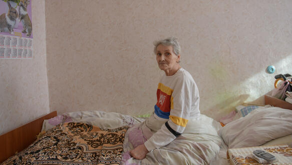 Das Bild zeigt das Porträtfoto einer Frau, die auf einem Bett sitzt 