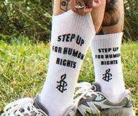 Man sieht eine Person, die weiße Socken und Sneaker trägt, auf den Socken steht "Step up for Human Rights"