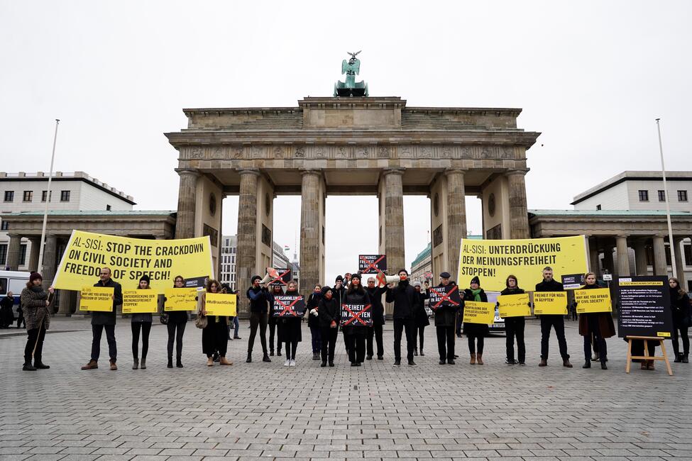 Eine Reihe schwarzgekleideter Menschen, die vor dem Brandenburger Tor Schilder und Transparente hochhalten