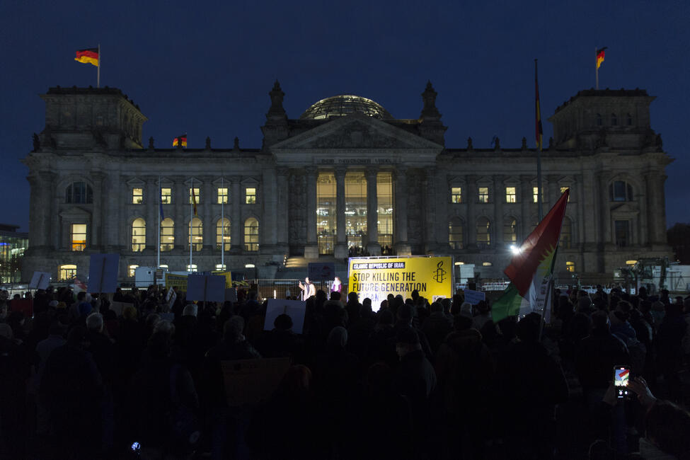 Das Bild zeigt den Deutschen Bundestag bei Nacht, davor steht eine Menschenmenge