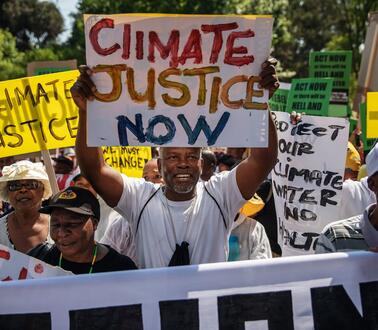 Eine Menschenmenge, in der viele Plakate hochhalten, auf denen die Menschen "Climate justice now", also "Klimagerechtigkeit jetzt" fordern. 