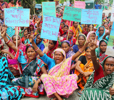 Das Bild zeigt mehrere Frauen, die auf dem Boden sitzen und Protestschilder halten.