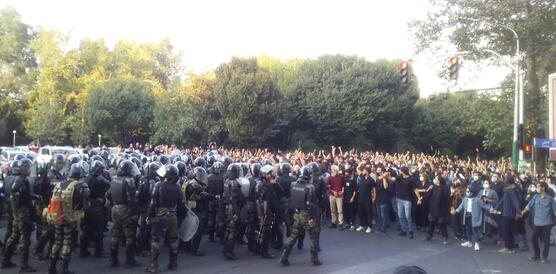 Das Bild zeigt eine große Menschenmenge auf der rechten Seite, links stehen viele bewaffnete Polizisten