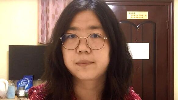 Eine junge chinesiche Frau mit schulterlangem Haar und einer drahtigen, rundenBrille schaut ernst in die Kamera.Im Hintergrund ein Büro.