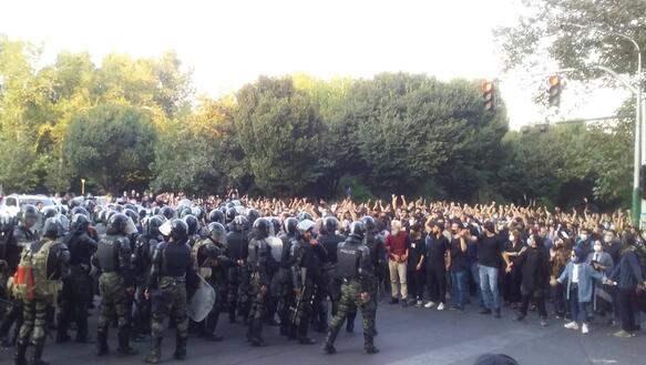 Das Bild zeigt eine große Menschenmenge auf der rechten Seite, links stehen viele bewaffnete Polizisten